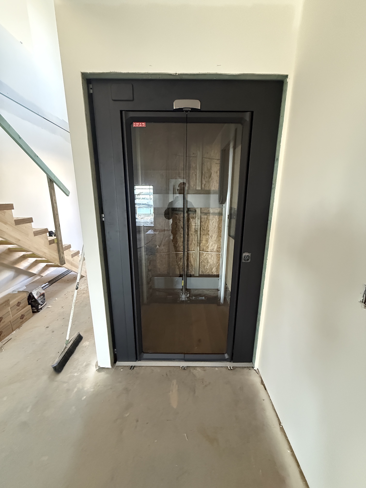 Black enclosed home lift installed beside the stairs of a two-storey Kiama Heights home
